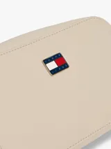 Cartera tipo bandolera Tommy Jeans de diseño compacto y acabado liso en color beige. Cuenta con cierre de cremallera superior y una insignia metálica distintiva de la marca en la parte frontal.