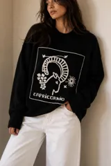Sweater de punto negro con diseño bordado a mano en el frente que representa el signo zodiacal de Capricornio con la palabra correspondiente, cuello redondo y mangas largas.