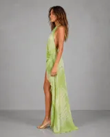 Vestido largo asimétrico de estilo etéreo, con escote halter cruzado y espalda descubierta. Presenta un diseño corto en la parte frontal y una cola larga en la parte posterior, confeccionado en una tela ligera con estampado abstracto en tonos verdes.