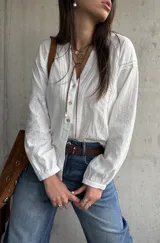 Camisa blanca de manga larga con detalles bordados en las mangas y encaje en el frente y hombros, escote en V con botones frontales.
