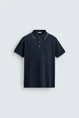 Remera polo de punto canalé color azul marino, de corte regular fit, con cuello solapa y cierre frontal de botones a presión. Cuenta con mangas cortas con ribetes blancos en los bordes del cuello y de las mangas.