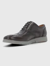 Zapato tipo Oxford estilo brogue con detalles perforados en la puntera y laterales. Presenta capellada de cuero en tono marrón oscuro, cordones al tono y suela de goma gris con diseño deportivo.