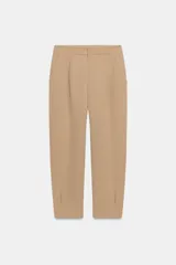 Pantalón de tiro medio con pinzas delanteras, bolsillos laterales y falsos bolsillos de vivo en la parte trasera. Presenta un corte holgado que se estrecha hacia el tobillo, con bajo acabado en pliegues y cierre frontal con cremallera, botón interior y gancho.