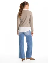 Buzo combinado marca Rio & Rian, con diseño de efecto capas que simula una camisa blanca debajo. Presenta un cuerpo de tejido de hilado fino en color beige con escote en V, y cuello y ruedo de gasa blanca.