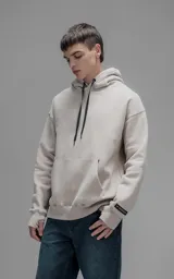 Hoodie oversize de color beige, confeccionado en frisa premium. Presenta capucha ajustable con cordones, bolsillo tipo canguro frontal y puños con aberturas para pulgares.