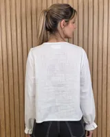 Camisa blanca de manga larga con volados en el escote en V y en los puños, con cierre frontal de botones oscuros.