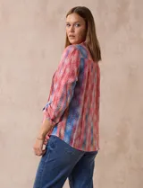 Blusa de gasa estampada multicolor, marca Ruby Rd. Tiene cuello a la base, escote en V, abertura central con botones y plisados en la parte delantera. Las mangas son 3/4 y tienen un largo regulable con presilla y botón.