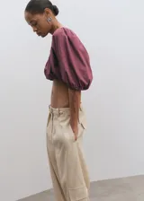 Blusa crop de color bordó, con diseño elástico fruncido, cuello redondo y mangas cortas abullonadas con lazo ajustable en los puños.