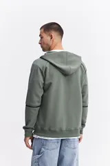 Campera con capucha y cierre frontal, color beige, con detalles de costuras y cierres en negro. Presenta mangas largas con puños acanalados y logo pequeño en el pecho.