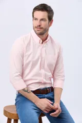 Camisa Oxford lisa de color celeste, con cuello abotonado, manga larga, cierre frontal de botones y un bolsillo aplicado en el pecho con detalle bordado.