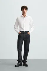 Camisa blanca de manga larga con cuello italiano abierto y cierre frontal de botonadura.