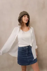 Camisa blanca de calce amplio, confeccionada en tejido liviano con sutiles rayas verticales, cuello clásico, mangas largas con hombros caídos y abotonadura frontal.