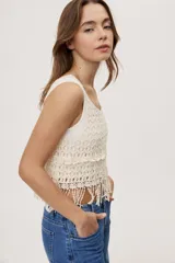 Top sin mangas de crochet color crudo, con escote redondo, diseño calado y terminación con flecos en el ruedo.