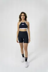 Top deportivo negro con ribete blanco, cuello halter y logo de la marca estampado en el frente.