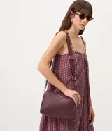 Cartera bandolera de tamaño mediano en cuero sintético color bordó, con formato rectangular y múltiples compartimentos con cierre de cremallera. Incluye correa de hombro ajustable en grosgrain y herrajes metálicos dorados.
