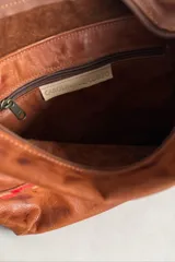 Cartera de cuero 100% natural color marrón, con diseño de hombro, cierre superior y detalles de arte pintado en la parte inferior.