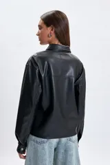 Sobrecamisa de cuero sintético en color negro, con cuello camisero, cierre frontal con botones metálicos a presión y mangas largas con puños abotonados.