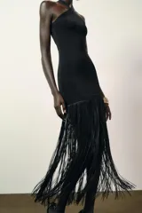 Vestido largo negro de tejido elástico, con escote halter y bajo con flecos a tono.