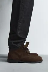 Bota tipo derby con cordones, confeccionada en piel con acabado de serraje. Presenta horma cuadrada y suela con ligero tacón.