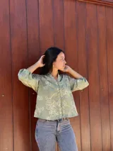 Camisa de corte holgado en color verde con estampado floral lineal en tono crema. Presenta cuello mao, cierre frontal con botones y mangas tres cuartos con puños elásticos.