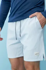 Short de baño con diseño de rayas verticales finas en color blanco y verde claro. Presenta cintura elástica con cordón ajustable y un parche decorativo con la inscripción 'motor oil' en el ruedo.