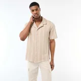 Camisa de manga corta color beige con diseño de rayas verticales blancas, cuello tipo cubano y cierre frontal con botones.