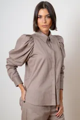Camisa de algodón color marrón con mangas largas abullonadas, cuello clásico y cierre frontal oculto. Presenta botones decorativos con strass en los puños y en el cuello.