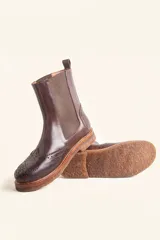 Bota tipo Chelsea de cuero vacuno color suela, con diseño brogue en la puntera y laterales. Presenta paneles elásticos laterales en color marrón oscuro, tirador trasero y suela de goma con plataforma.