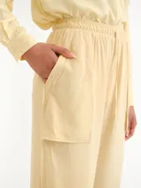 Pantalón de corte ancho, color amarillo claro, con cintura elástica fruncida y cordón ajustable. Cuenta con bolsillos frontales aplicados y dobladillo ancho en los tobillos.