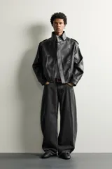Cazadora biker relaxed fit confeccionada en tejido efecto piel, color negro. Cuenta con cuello subido, manga larga con puño ajustable y bajo elástico. Incluye bolsillos de vivo en la cadera y cierre frontal con cremallera oculta bajo una solapa diagonal con botones a presión.