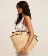 Bolso de playa tipo tote de paja natural con asas de cuero sintético marrón, forro interior y bolsillo interno.