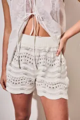 Short tejido de punto con diseño de ondas y calados, color blanco. Presenta cintura elástica acanalada y corte mini.