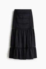 Pollera larga de color negro con elegantes alforzas e inserciones de encaje. Modelo de corte holgado con cintura elástica en la parte posterior.