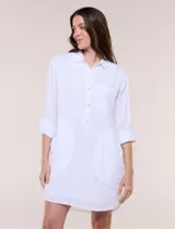 Vestido camisero corto de color blanco con sutiles rayas verticales, de la marca Dash. Presenta cuello con solapa, escote en V con botones parciales en el frente, bolsillo superior en el pecho y bolsillos laterales de gran tamaño. Cuenta con mangas largas de largo regulable mediante presilla y botón, calce holgado y ruedo trasero más largo.