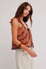 Musculosa blanca de poliéster con diseño romántico, tirantes con volados, detalles de encaje y cierre frontal con cordón ajustable y botones.