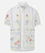 Camisa de lino y algodón color blanco con cuello inglés, manga corta y cierre frontal de botones. Presenta un diseño de bordado fino floral y de aves de estilo artesanal.