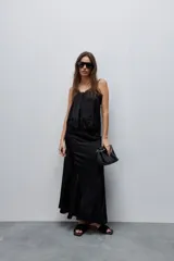Falda larga de color negro, calce al cuerpo y caída fluida, confeccionada en tejido satinado con detalle de recorte diagonal en la parte delantera y cintura elástica.