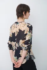 Camisa de manga larga con fondo verde y estampado floral en tonos rosados y beige, cuello redondo con pequeña abertura en V y cierre frontal con botones.