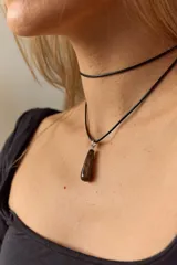 Gargantilla de cuero negro con dije de piedra blanca en forma de lágrima con engarce dorado.