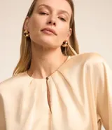 Blusa celeste de tejido satinado con cuello redondo, pliegues en el cuello y manga corta.