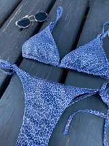Traje de baño de dos piezas con estampado animal print en tonos azules y negros. El corpiño es de corte triangular con tirantes finos y la bombacha es colaless con tiras laterales ajustables.
