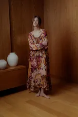 Maxi vestido estilo boho con estampado floral en tonos rosa, naranja y borgoña. Tiene mangas largas sueltas, escote redondo con volados y falda larga con volados.