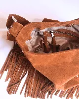 Cartera tipo shoulder bag de cuero gamuzado color suela, con diseño de flecos en la base y detalle de tachas metálicas en los laterales. Cuenta con correa regulable y forro interior.