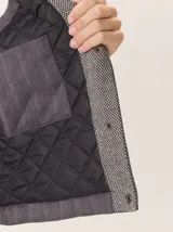 Chaleco con capucha, presenta una espalda de pelo sintético en color marrón oscuro con etiqueta de cuero negra y una capucha de tela tipo denim azul. Diseño original con mezcla de texturas.