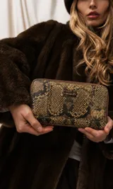 Billetera larga tipo portafolio con cierre perimetral, confeccionada en material sintético con estampado de imitación piel de serpiente en tonos marrones y beige. Cuenta con una placa metálica frontal con el grabado de la marca "Lincoln's".