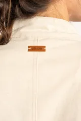 Chaqueta corta color beige de algodón, de inspiración militar con cuello mao y doble botonadura frontal con botones metálicos dorados.