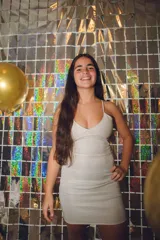 Vestido corto de fiesta color plateado con acabado brillante. Presenta un diseño de dos piezas que simula un conjunto de top y pollera, con aberturas laterales en la cintura, escote en V y tirantes finos que se cruzan en la espalda.