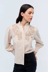 Camisa color crema a rayas verticales con bordado floral en el pecho, cuello mao y mangas largas abullonadas con puños elásticos.