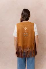 Chaleco de gamuza sintética color tostado, con diseño abierto sin cierre, detalles de calados geométricos y terminación con flecos largos en el ruedo.