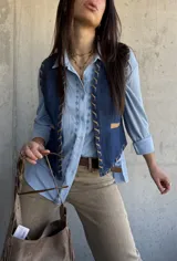 Chaleco de denim azul oscuro con detalles de costuras decorativas y ribetes en tono tostado.